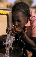 Young girl drinks fresh water from a pump